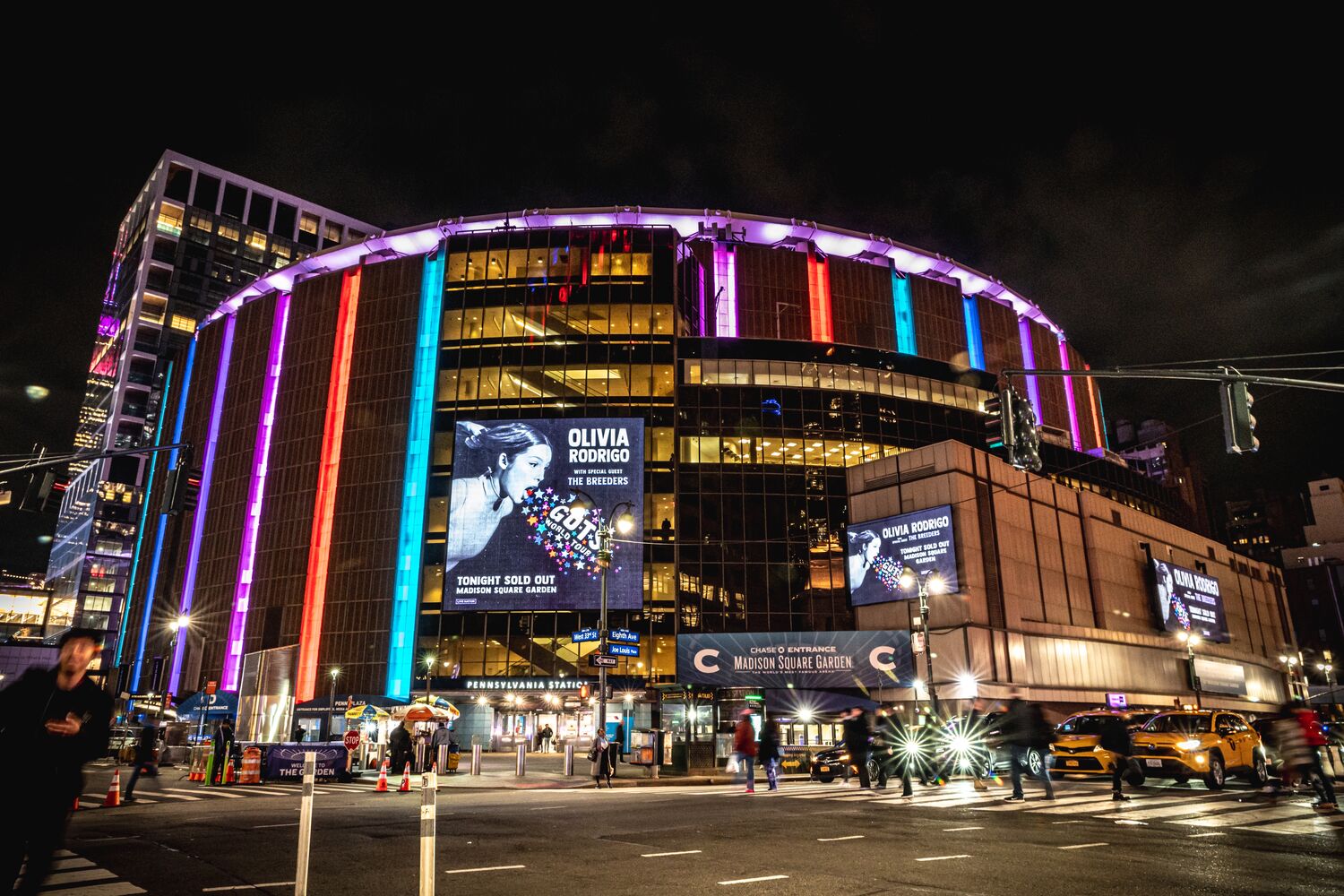 Madison Square Garden at night, its curved facade lit in purple, red and blue, with Olivia Rodrigo's sold-out show on the marquee screens.